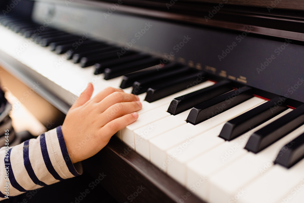 Obraz premium Pretty 3-year-old girl plays the keys of a piano and reads the sheet music with difficulty.