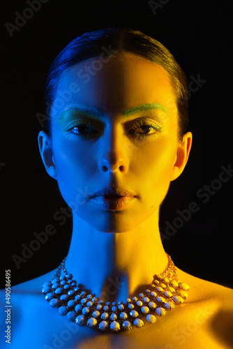 A woman s face in the blue and yellow national colors of Ukraine looks at the camera isolated on a dark background. Flag of UA  no war.