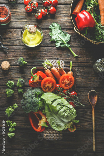 Various colorful vegetables on wooden plate, kitchen utensils and ingredients: cabbage, tomatoes,broccoli,carrots, bell pepper, olive oil at rustic wooden kitchen table. Top view. Healthy food