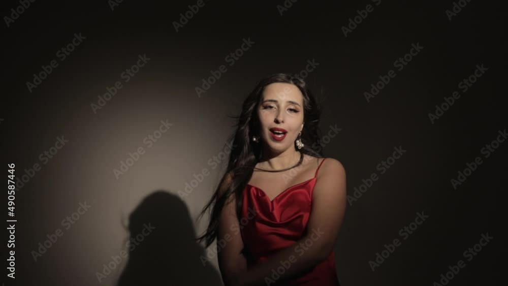 A brunette girl in a red dress sings in the twilight. The wind blows the hair. A brunette girl in a red dress sings in the twilight. The wind blows the hair.