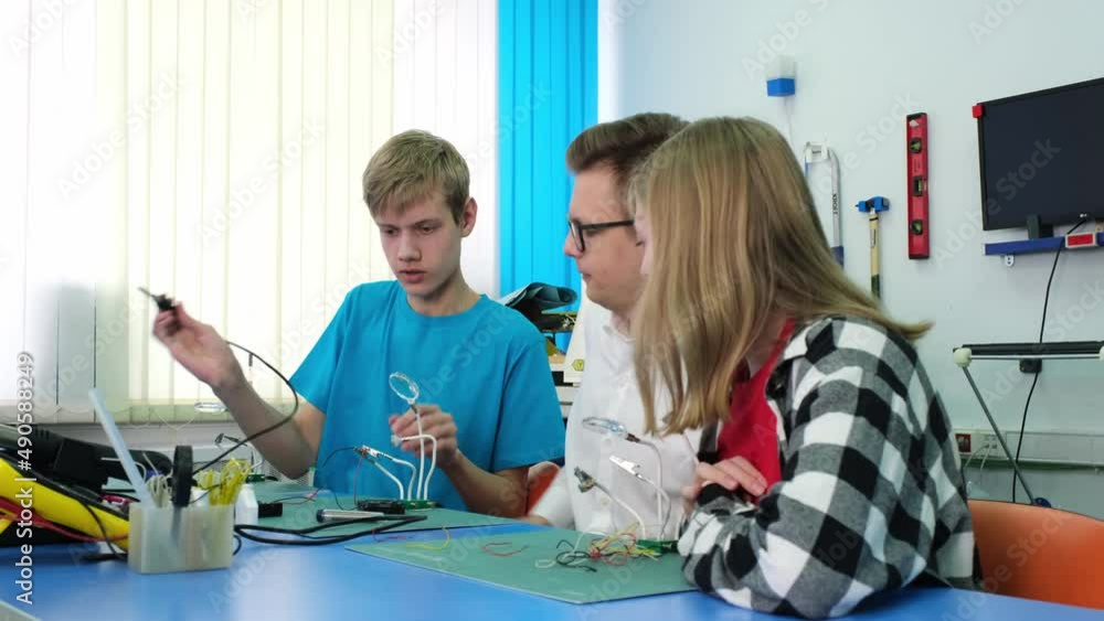 The teacher teaches the boy how to work with an electric soldering iron The teacher teaches the boy how to work with an electric soldering iron