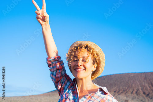 Victory hand gesture to stop war and love peace for people concept image with happy adult woman in the country side  smiling and enjoying the day. Environment and good future for earth supporter