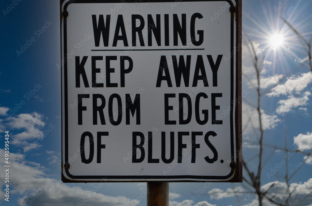 Warning Sign for Bluffs against a cloudy sky with a starburst Warning Sign for Bluffs against a cloudy sky with a starburst