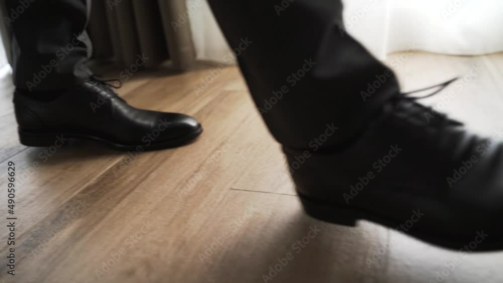 Man in black leather shoes and dress pants walks across the room. Close-up male legs stepping on the floor during the day Man in black leather shoes and dress pants walks across the room. Close-up male legs stepping on the floor during the day