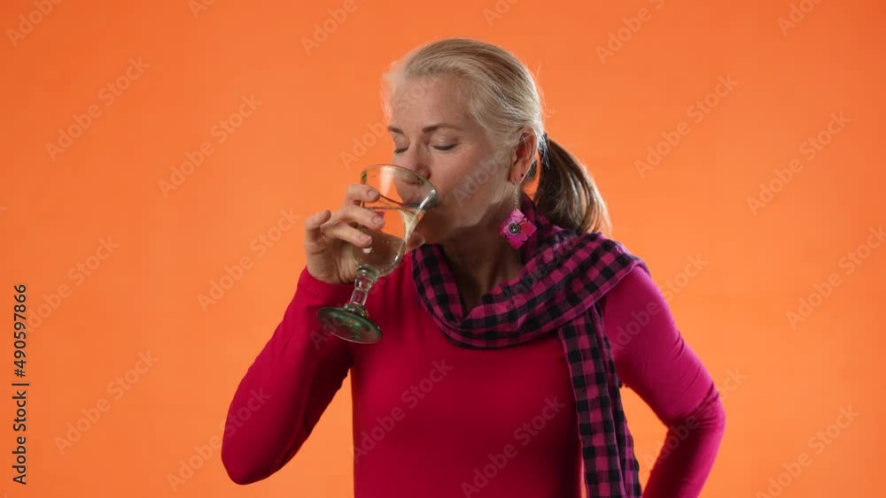 Beautiful smiling happy blond mature woman holding wineglass and drinking wine on solid orange background with copy space. Beautiful smiling happy blond mature woman holding wineglass and drinking wine on solid orange background with copy space.