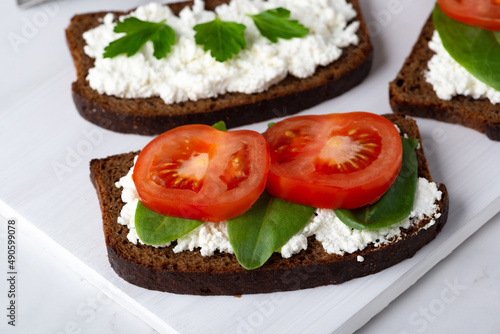 Slice of rye bread with cottage cheese and tomatoes on a wooden cutting board