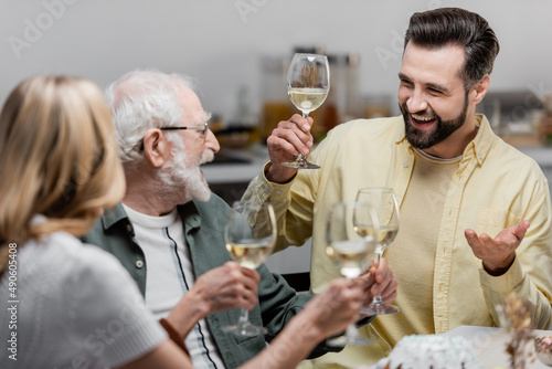 senior man holding glass of wine while celebrating easter with adult son and daughter.