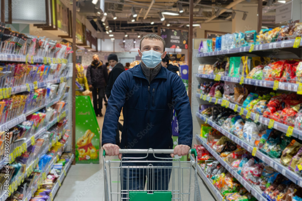 A man wearing a protective face mask in a shopping mall. A customer walking with a cart in a supermarket
