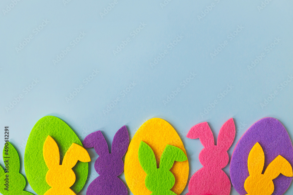 Colorful Easter bunnies and eggs on blue background, top view with space for text. Happy Easter! Pink, yellow, purple artificial bunny and egg decor. Easter hunt concept