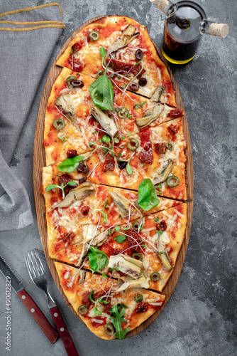 Vegetarian long pizza with artichokes, dried tomatoes, olives and basil on a gray concrete background. Italian dish pizza made of dough with vegetables, top view