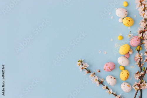 Easter flat lay with space for text. Colorful Easter chocolate eggs with cherry blossoms on blue background. Happy Easter  Stylish tender spring template. Greeting card or banner