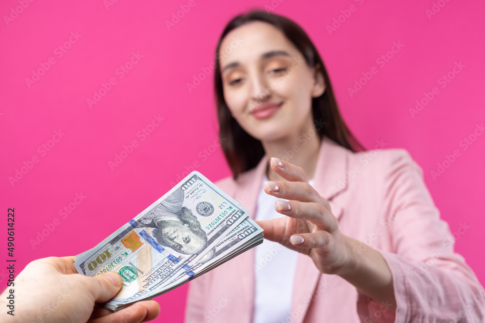 A woman in a pink jacket receives a bribe in dollars against a red background. A woman in a pink jacket receives a bribe in dollars against a red background.