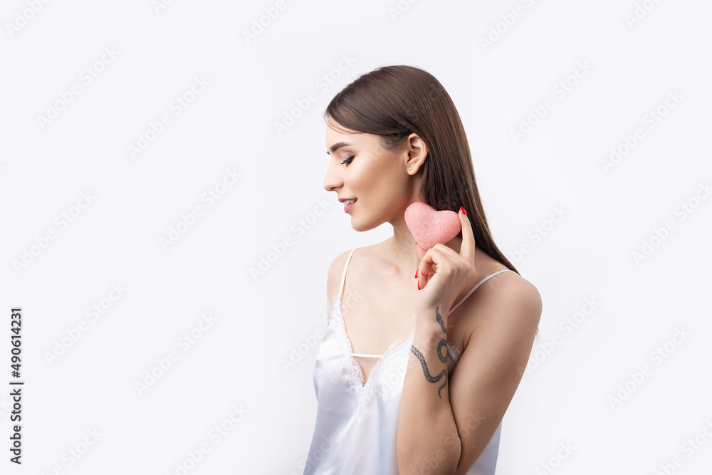 Beautiful smiling woman with clean skin, natural make-up and white teeth on a gray background. Holding a pink hygienic heart. Beautiful smiling woman with clean skin, natural make-up and white teeth on a gray background. Holding a pink hygienic heart.