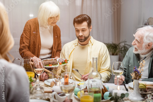 Photography senior woman holding fried meat near adult son during easter family dinner