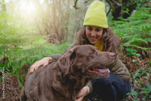 smiling pretty young woman in yellow hat playing with her labrador retriever breed dog in the forest at sunset. stock photography
