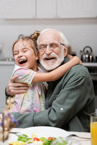 excited girl with closed eyes embracing happy grandfather during easter celebration. photo