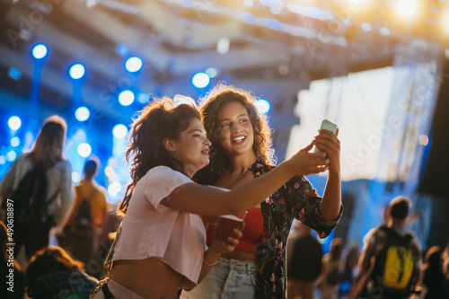 Two beautiful friends taking selfie with a samrtphone on a music festival