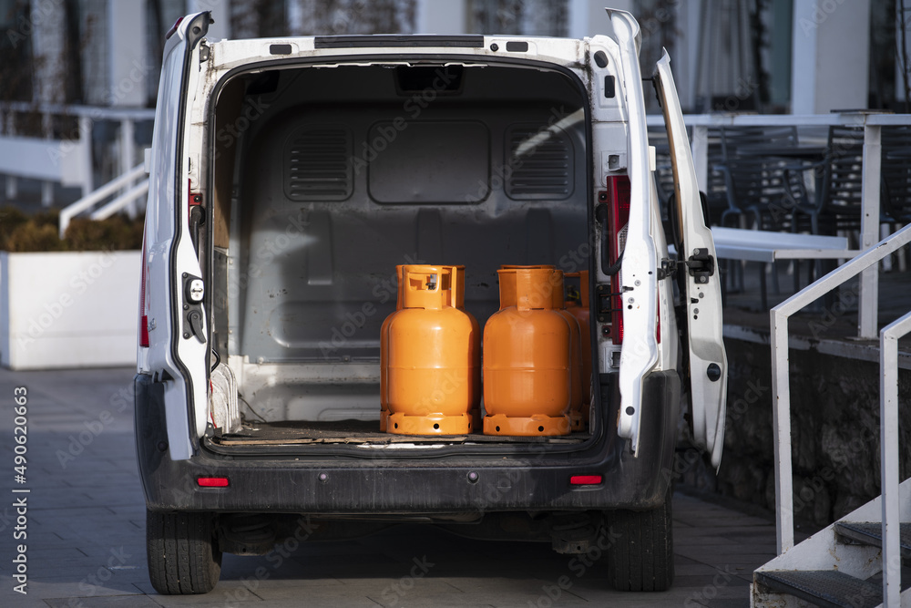 Orange gas cylinders transported inside a pickup car. Gas butane bottles in truck ready for delivery. Vehicle delivering hazard goods with compressed gas. Orange gas cylinders transported inside a pickup car. Gas butane bottles in truck ready for delivery. Vehicle delivering hazard goods with compressed gas.