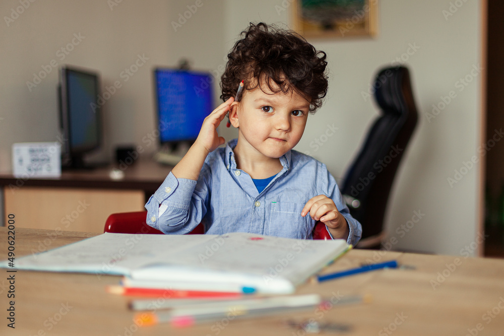 Preschool education online. A cheerful and energetic preschooler at the computer is engaged, next to notebooks, pencils. Lesson with a teacher remotely. Preschool education online. A cheerful and energetic preschooler at the computer is engaged, next to notebooks, pencils. Lesson with a teacher remotely.