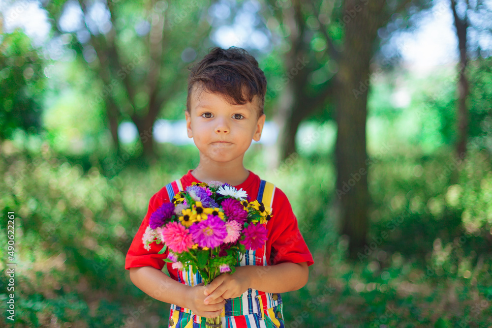 Smiling boy with a bouquet of wildflowers, a surprise for mom in the holiday. A child with flowers in bright clothes. red T-shirt in nature with a bouquet of chrysanthemums and daisies Smiling boy with a bouquet of wildflowers, a surprise for mom in the holiday. A child with flowers in bright clothes. red T-shirt in nature with a bouquet of chrysanthemums and daisies