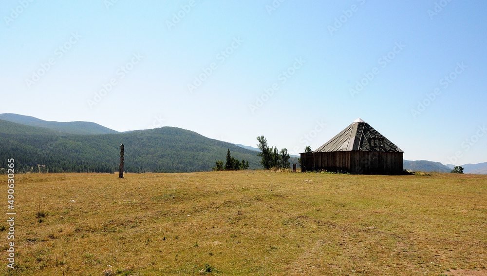 Wooden one-story house and hitching post on top of a hill overlooking high mountain ranges.