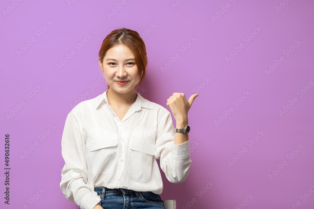 Confident young woman with assured smile pointing left at copy space logo, showing good deal, recommending product, purple background. Confident young woman with assured smile pointing left at copy space logo, showing good deal, recommending product, purple background.