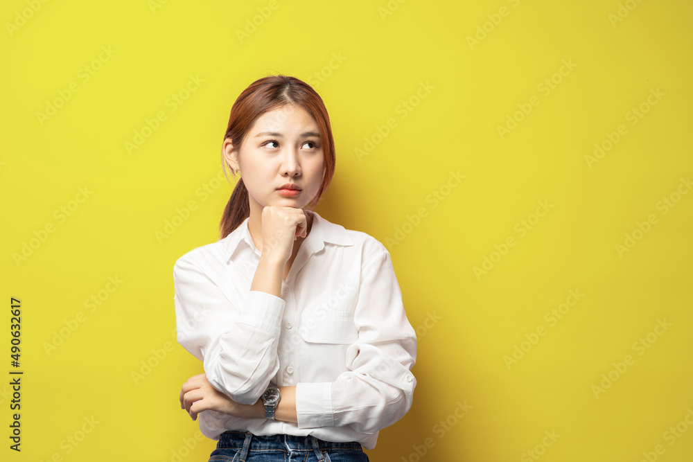 Portrait of thoughtful smart asian woman thinking, female student solving puzzled, look up complicated or pondering, touch chin while trying made up idea, daydreaming over yellow background. Portrait of thoughtful smart asian woman thinking, female student solving puzzled, look up complicated or pondering, touch chin while trying made up idea, daydreaming over yellow background.