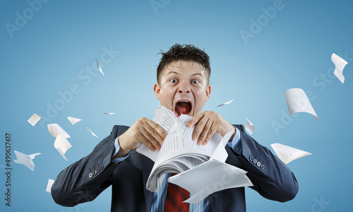 Young stressed man ripping documents with frustrated facial expression.