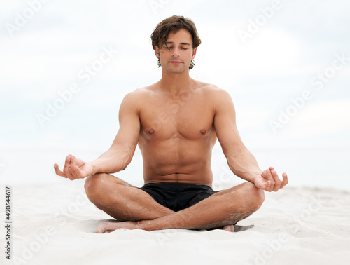 Be still and listen to what nature has to say. Young handsome man sitting on the beach meditating.