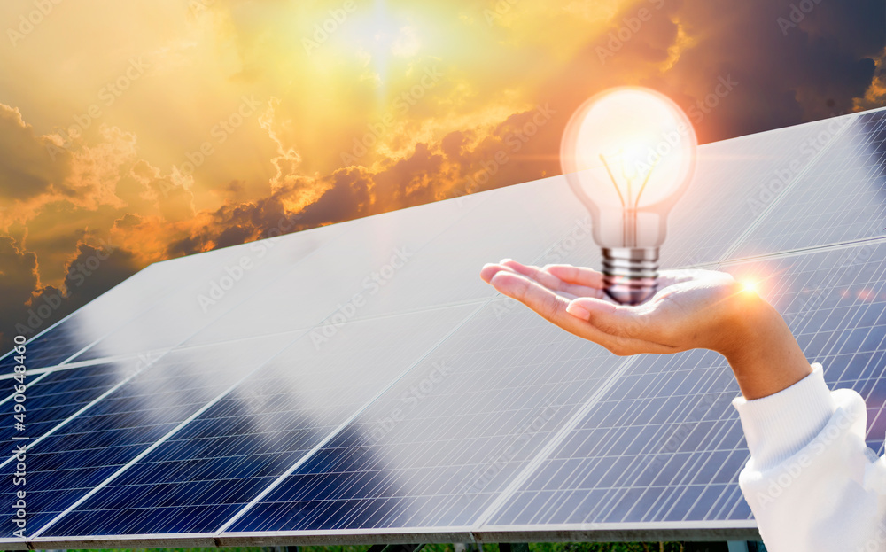 Woman holding a white light bulb in a solar panel background. . Solar panels  and energy-saving lamps. Clean energy concept. Stock Photo | Adobe Stock