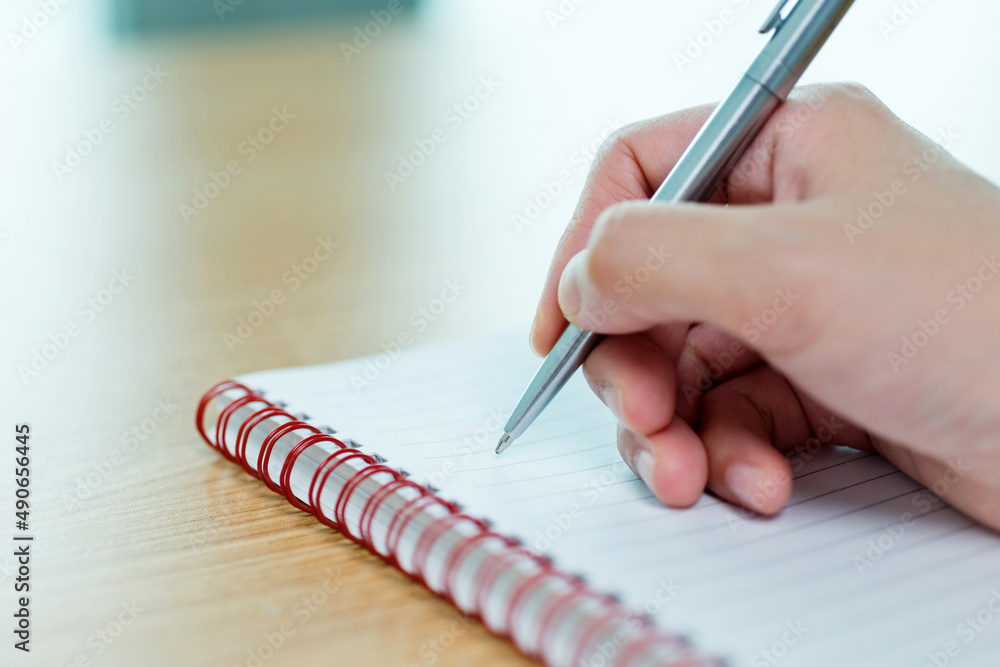Hand writing in spiral notepad on wooden table Hand writing in spiral notepad on wooden table