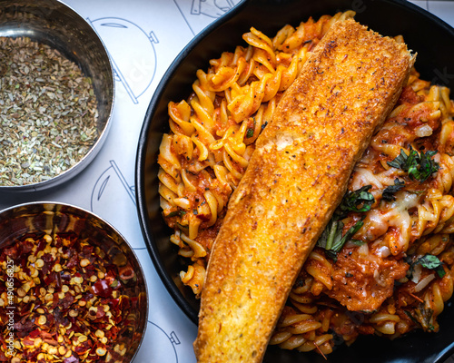 Selective focus of Fusilli Arrabiata pasta and a slice of bread served on black iron pan. 