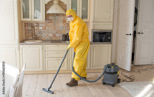 a man in a protective suit cleans the room with a vacuum cleaner.