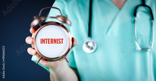 Internist (Arzt für innere Medizin). Arzt zeigt Wecker/Uhr mit Text. Hintergrund blau. photo