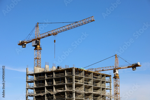 Construction tower cranes above unfinished residential building on blue sky background. Housing construction, apartment block