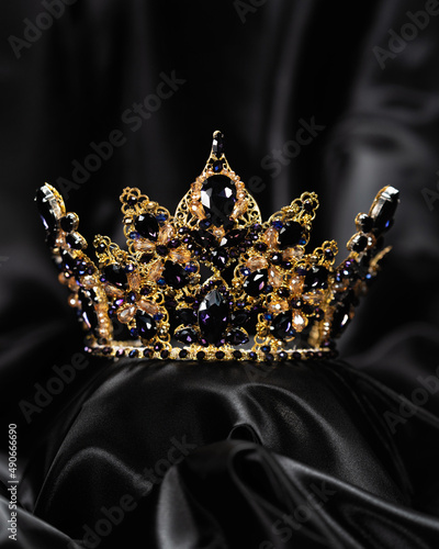 Crown for miss beauty, a symbol of power and elegance, competition, show. Diadem in yellow metal and blue stones on a black draped satin background