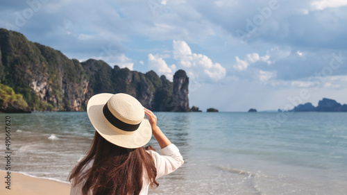Rear view image of a young woman with hat walking on the beach with blue sky background