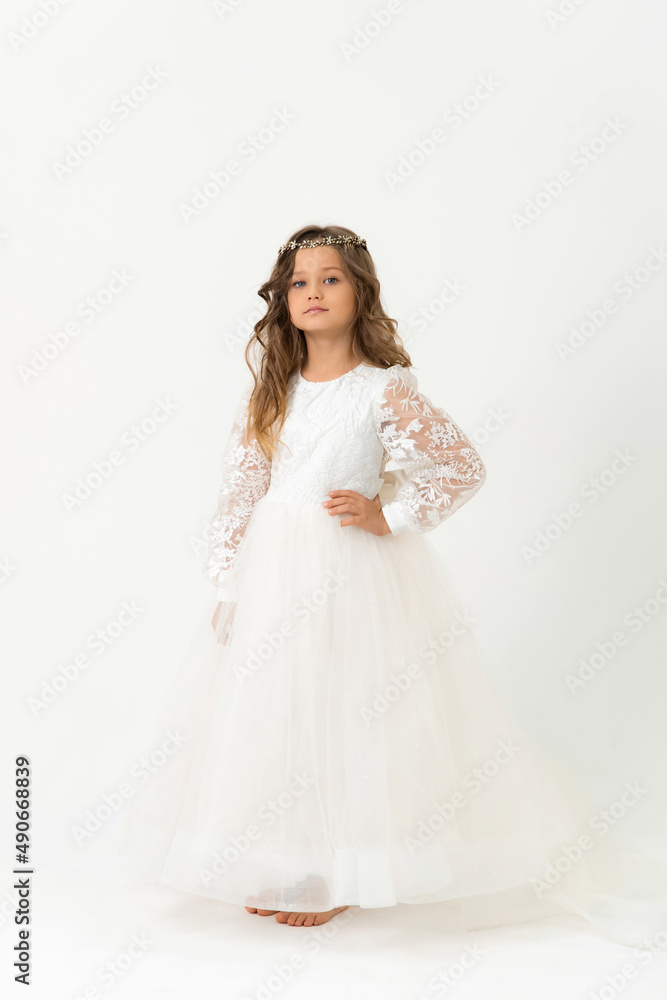 A beautiful six-year-old girl is posing, looking at the camera. Studio portrait. White background