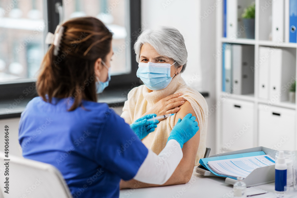 Obraz premium medicine, health and vaccination concept - doctor or nurse with syringe making vaccine or drug injection to senior woman in mask at hospital