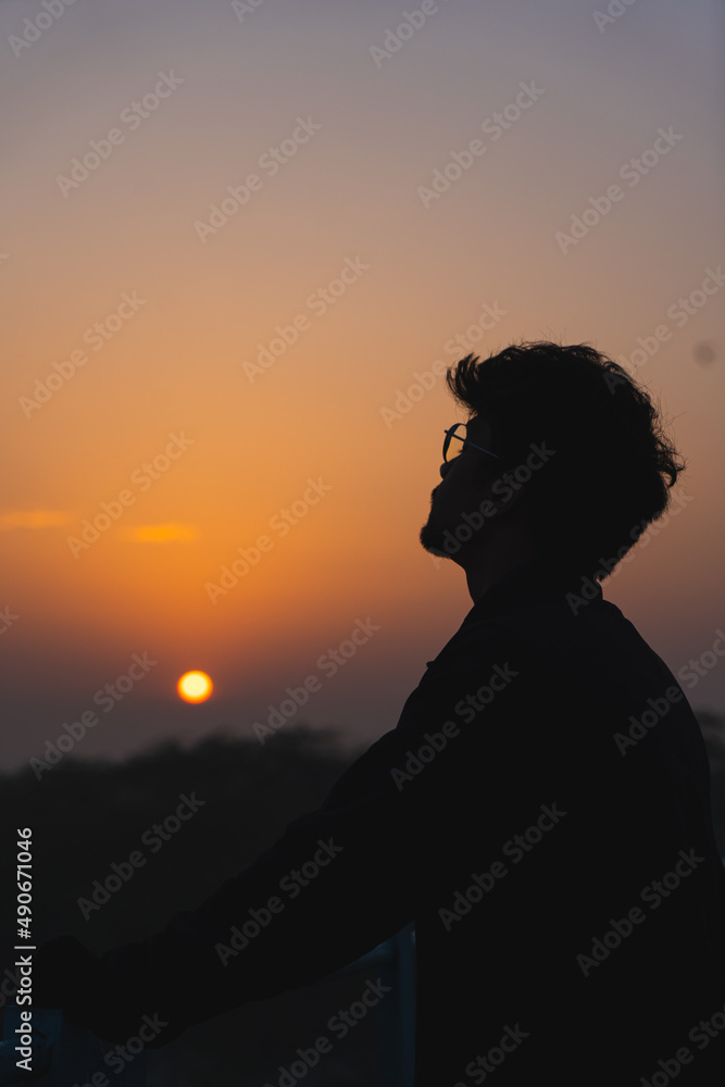 Silhouette of a young boy wearing specs enjoying the beautiful sunset.