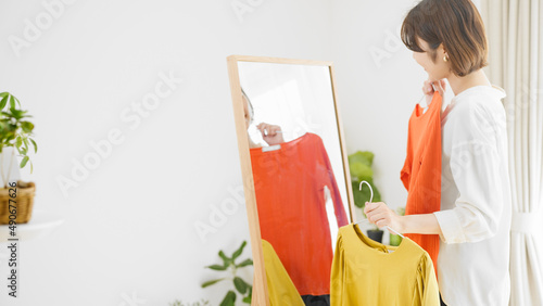 鏡の前で服選びをしている若い女性　ファッションイメージ