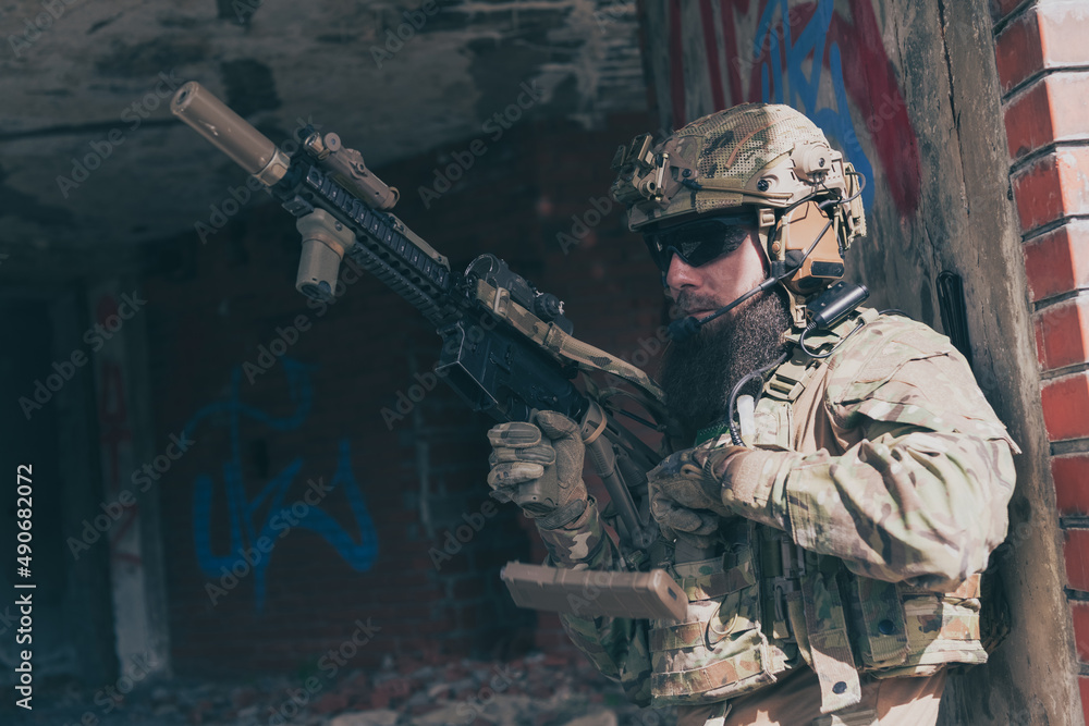 A bearded soldier in special forces uniform in dangerous military mission, refile his weapon while hiding from the wall. Selective focus A bearded soldier in special forces uniform in dangerous military mission, refile his weapon while hiding from the wall. Selective focus