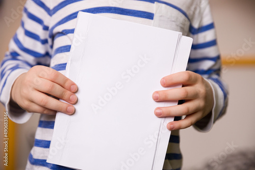 A boy in a striped sweater holds blank sheets of paper in his hands. Close-up
