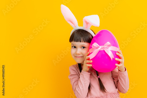 Canvas Print Cute baby little girl with bunny ears holding a big Easter egg on a colored yell