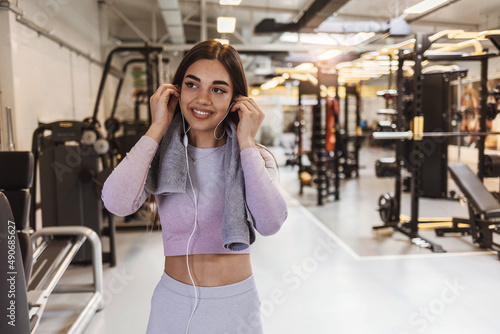 Shot of an attractive young woman taking a break from her workout in the gym. Happy athletic woman with the towel and listening music while exercising in a gym. People, sport and fitness concept