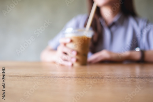 Closeup blurred image of a young woman holding and drinking iced coffee