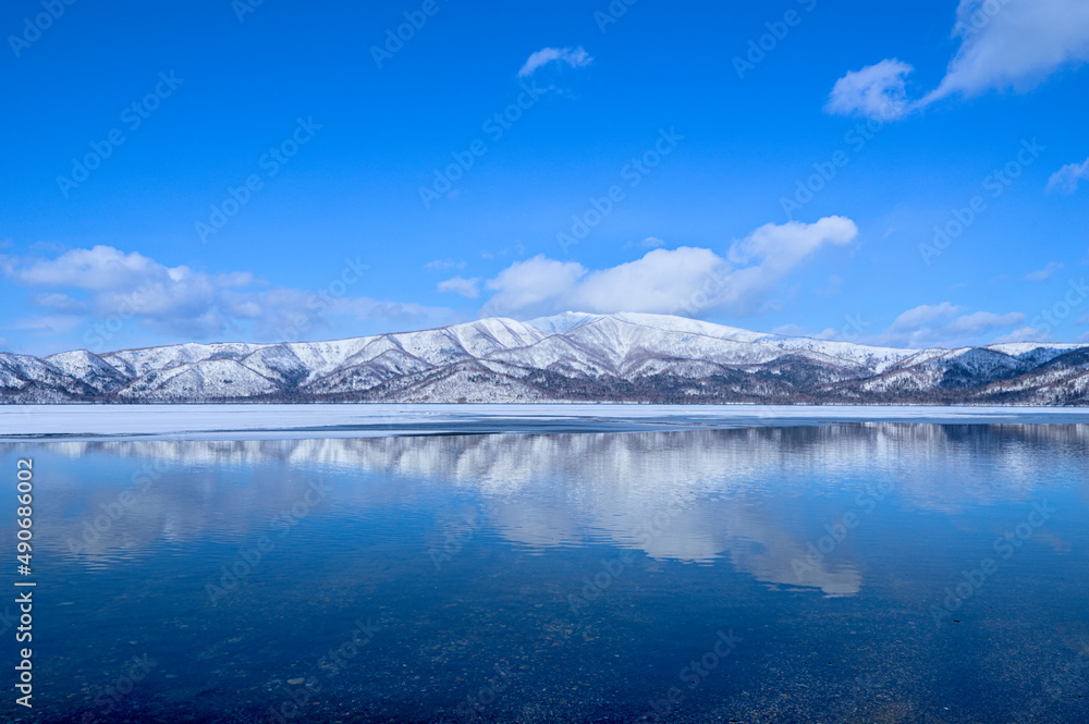 鏡の湖に反射する青空と雪山。冬の北海道の屈斜路湖。