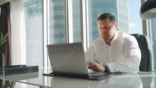 Nervous look of a businessman sitting at a table in the office. Online trading. Successful and young trader in a white shirt working with a laptop while sitting in his office in front of a laptop