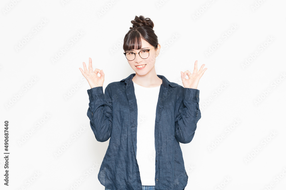 白い背景の前に立ってOKのジェスチャーをする眼鏡をかけている女性 白い背景の前に立ってOKのジェスチャーをする眼鏡をかけている女性