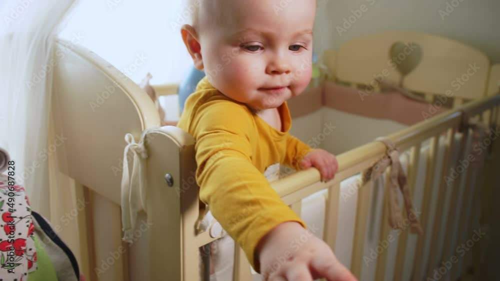 baby stands in crib and pulls her hand to camera baby stands in crib and pulls her hand to camera